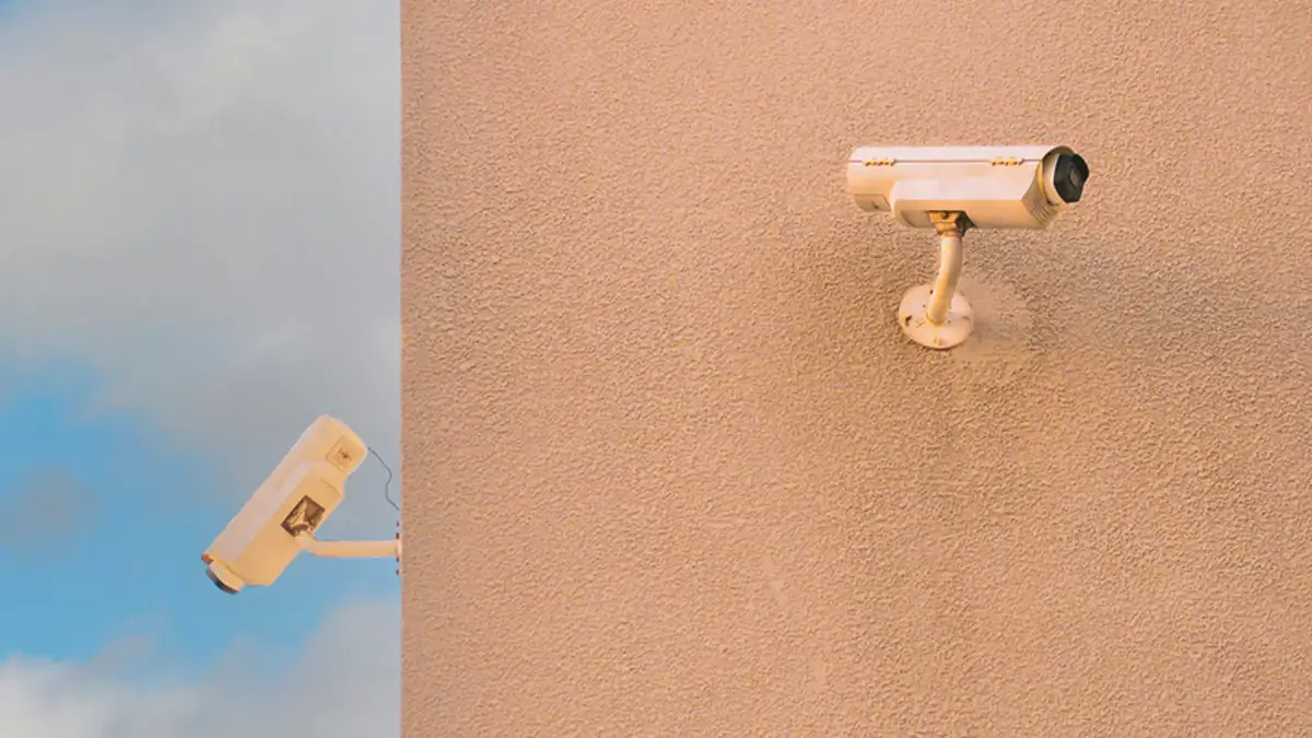Two cream-coloured security cameras mounted on a peach stucco wall against a blue sky