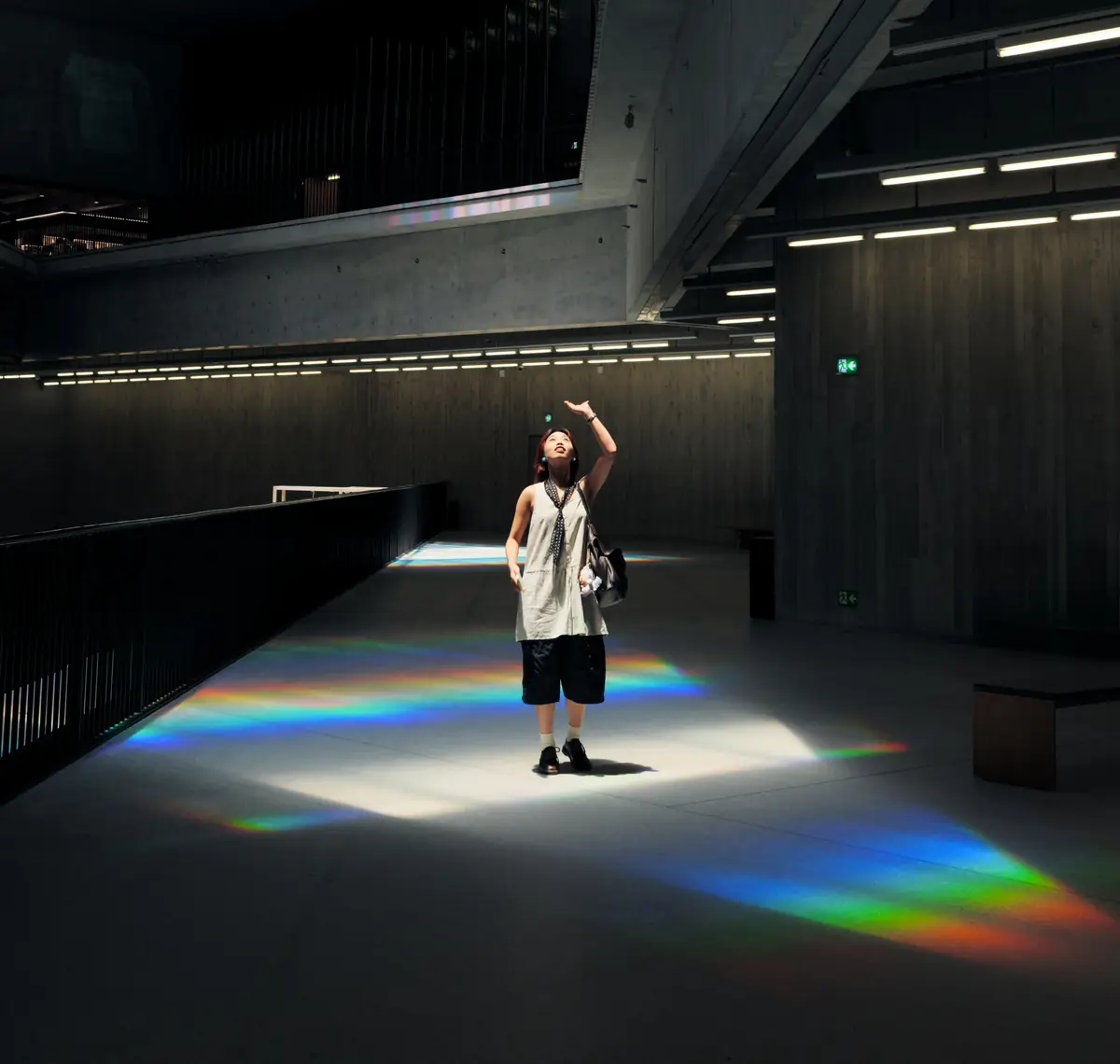 A visitor in the concrete atrium of M+ in Hong Kong looks up as light from a skylight scatters into rainbows across the floor